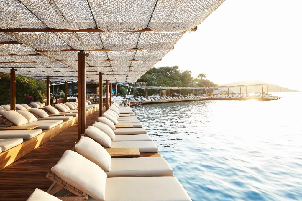 Luxury wooden sun loungers with beige cushions lined up on a beach club pier by Outex